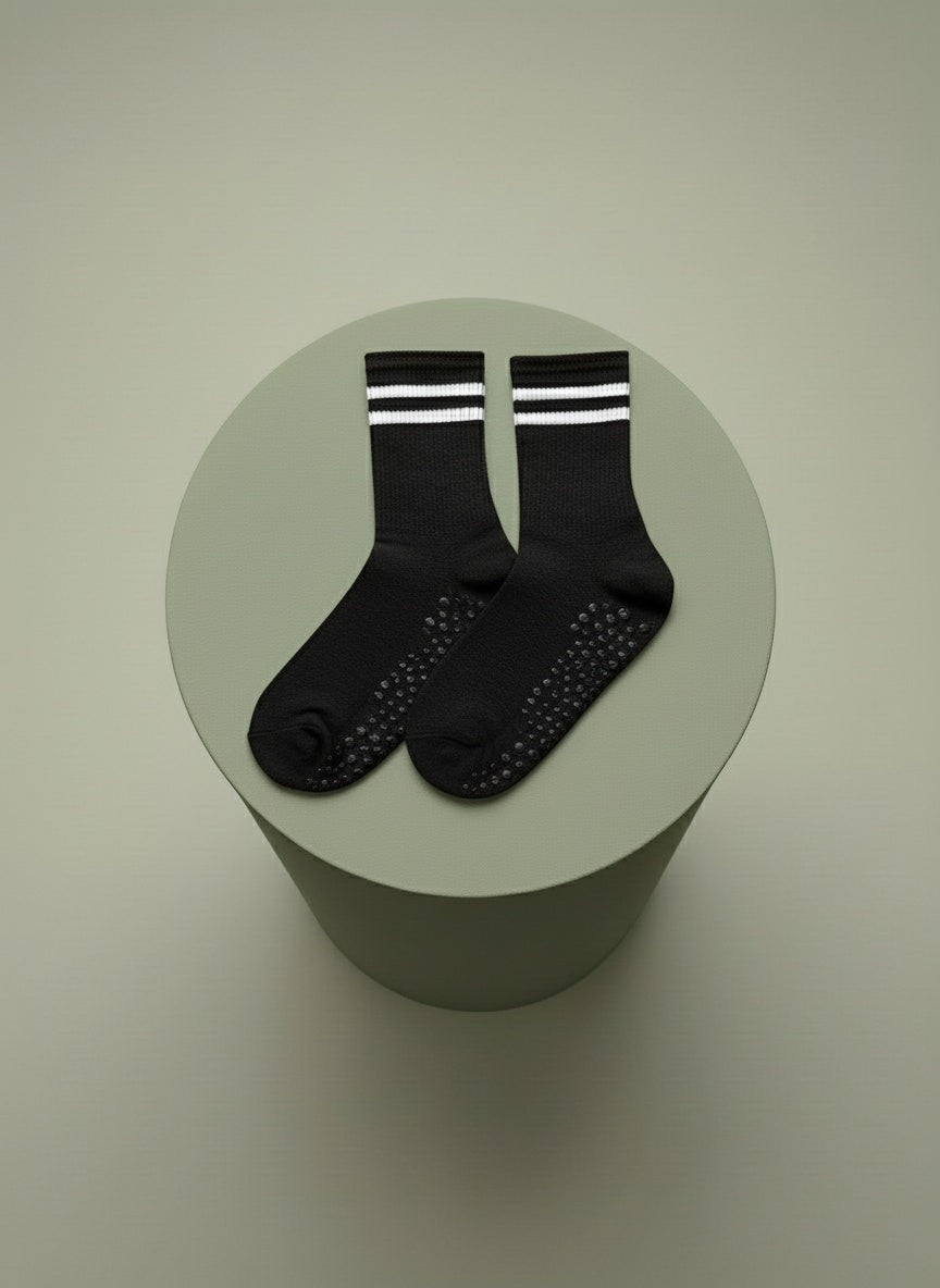 Svarta pilatesstrumpor med vita revärer ligger på grön bakgrund