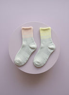 Pilates strumpor med grepp i vit, gul och rosa färg liggandes på rosa bakgrund