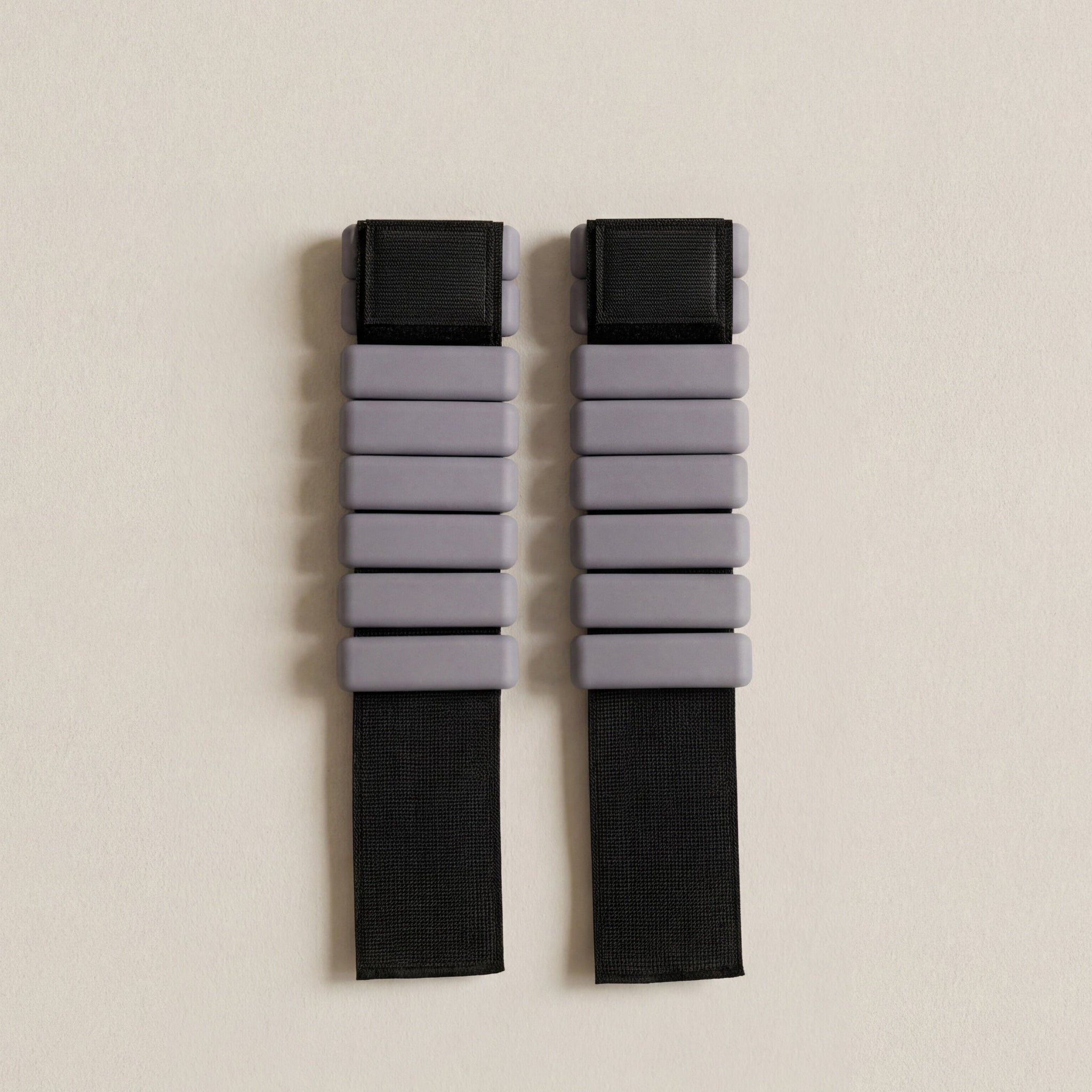 grå pilates vikter för ankel och handled med svart straps liggandes på beigt golv