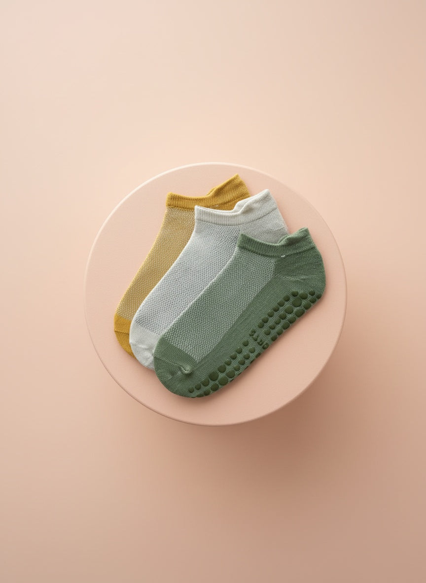 Låga ankelstrumpor för pilates i orange, vit och grön färg liggandes på beige bakgrund