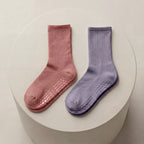 Rosa och lila antihalkstrumpor med greppskydd liggandes på beige cylinder
