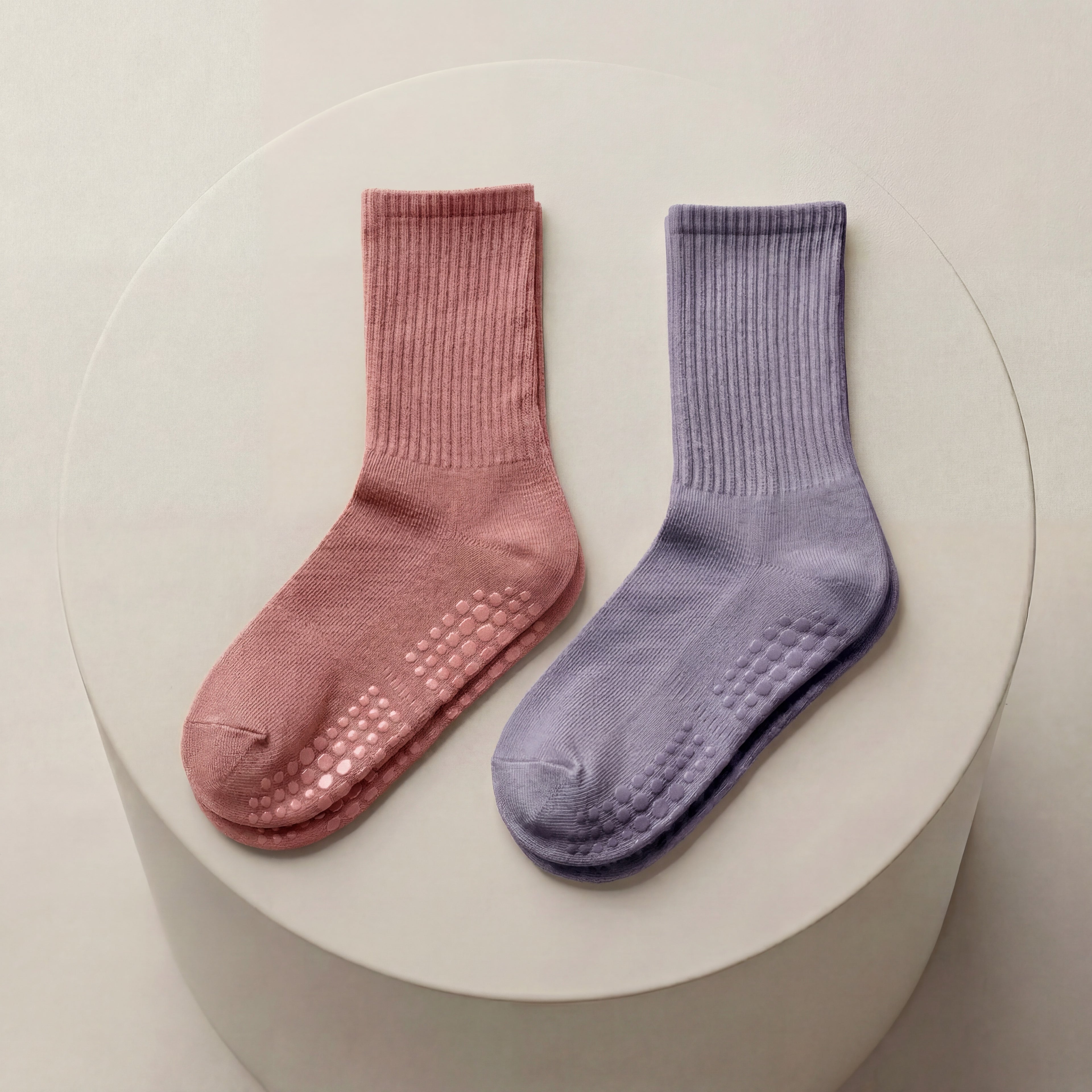 Rosa och lila antihalkstrumpor med greppskydd liggandes på beige cylinder
