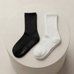 Svarta och vita antihalkstrumpor med greppskydd liggandes på beige cylinder