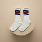 Vita pilates strumpor med grepp för kvinnor med röda och blåa ränder sitter på en beige cylinder