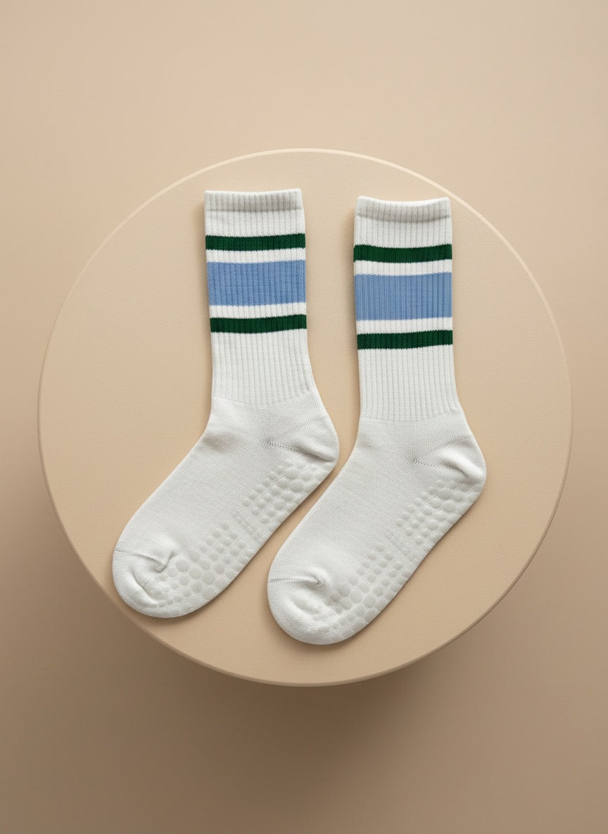 Höga pilates strumpor för damer i vitt med gröna och blå ränder i toppen liggandes på beige bakgrund