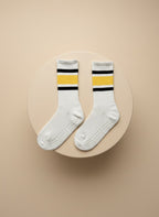 Vita pilatesstrumpor för träning med gula och svarta ränder för träning ligger på en beige cylinder