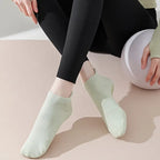 Kvinna som har på sig ett par gröna pilatesstrumpor för yoga med grepp undertill, kvinnan håller i ett träningsredskap